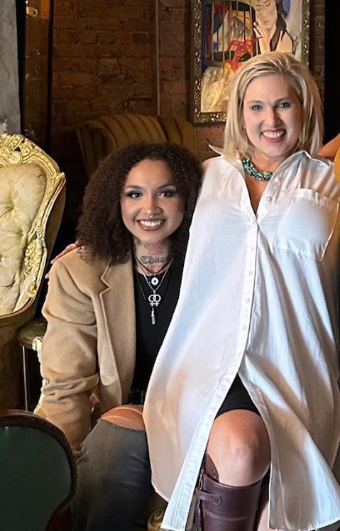 Two women posing for a picture in front of a chair.