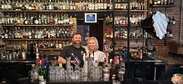 A man and woman standing behind a bar.