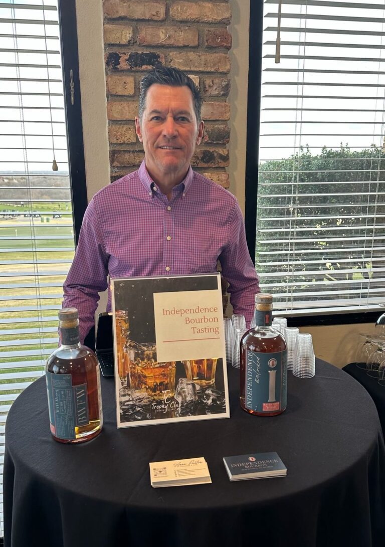 A man standing at a table with two bottles of alcohol.