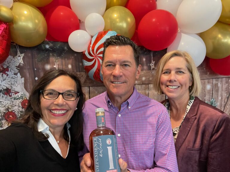 Three people holding a bottle of wine in front of balloons.